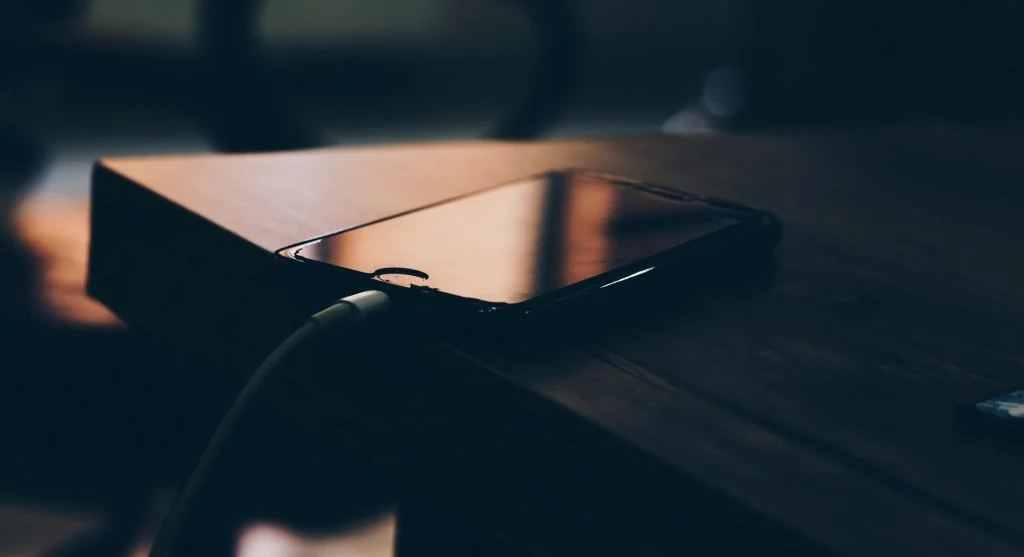 A person charging their phone at night with a clock in the background