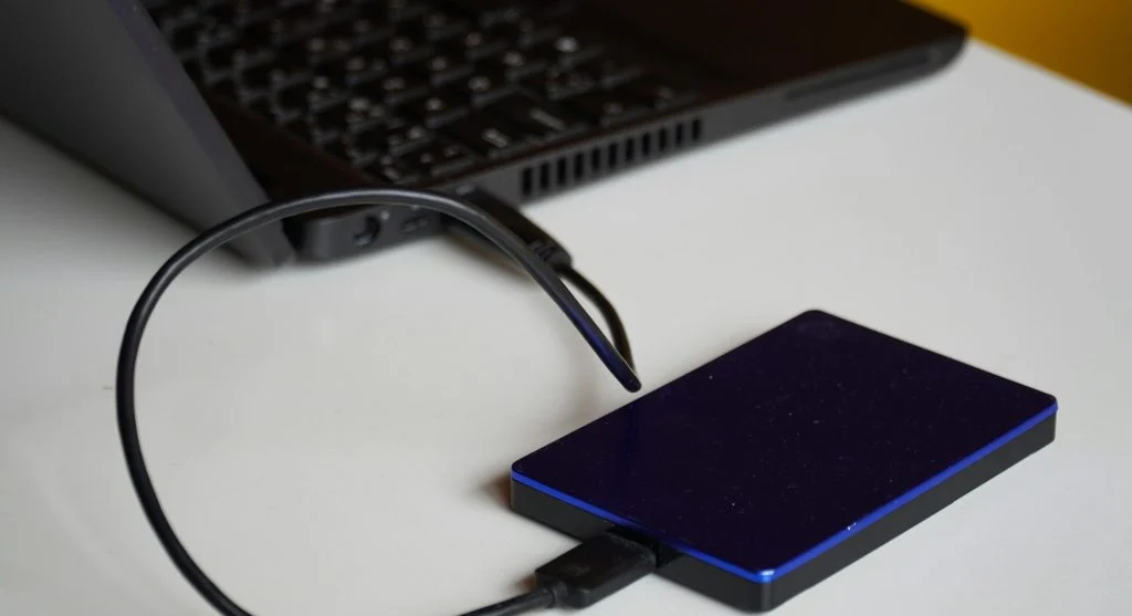 Person connecting an external hard drive to a laptop with a cloud icon in the background
